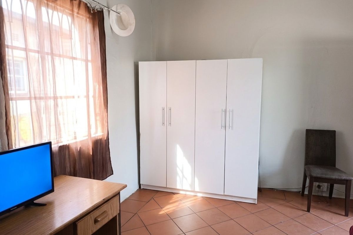 A bedroom featuring tiled flooring and a white built-in wardrobe, offering a functional space with natural light from the window.