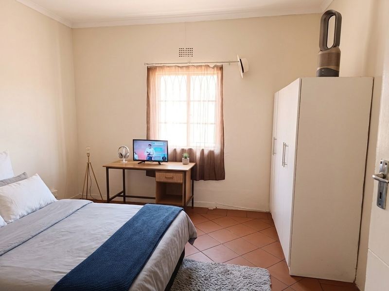 A functional bedroom featuring tiled flooring, a built-in wardrobe, and natural light through a window.