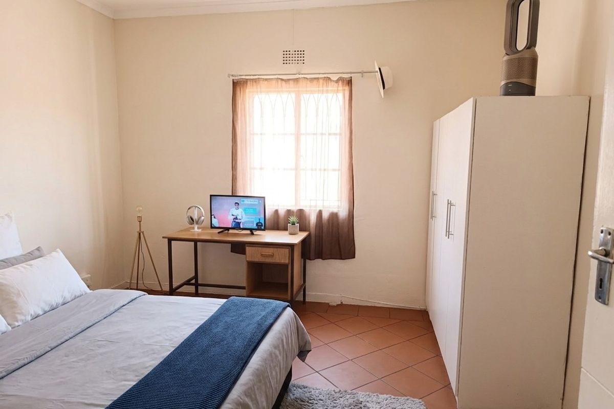 A functional bedroom featuring tiled flooring, a built-in wardrobe, and natural light through a window.