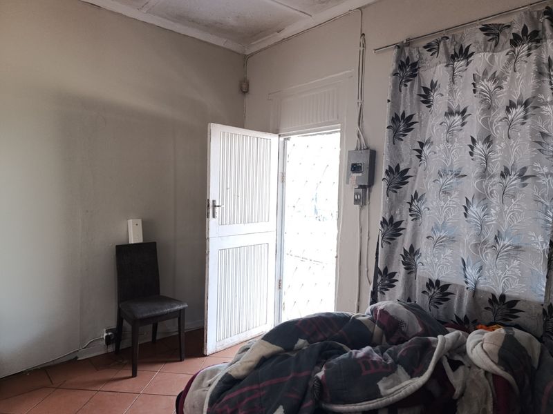 A bedroom featuring tiled flooring, an exposed electrical distribution board, and a panel door leading to the exterior.