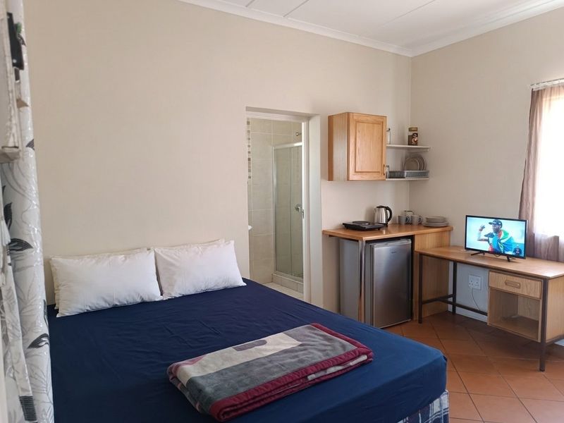 A functional bedroom featuring tiled flooring and an attached en-suite bathroom with a shower cubicle.