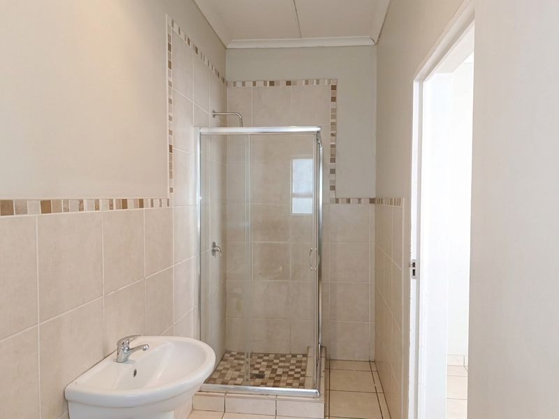 A clean and functional bathroom featuring a glass shower enclosure, pedestal basin, and neutral wall and floor tiling.