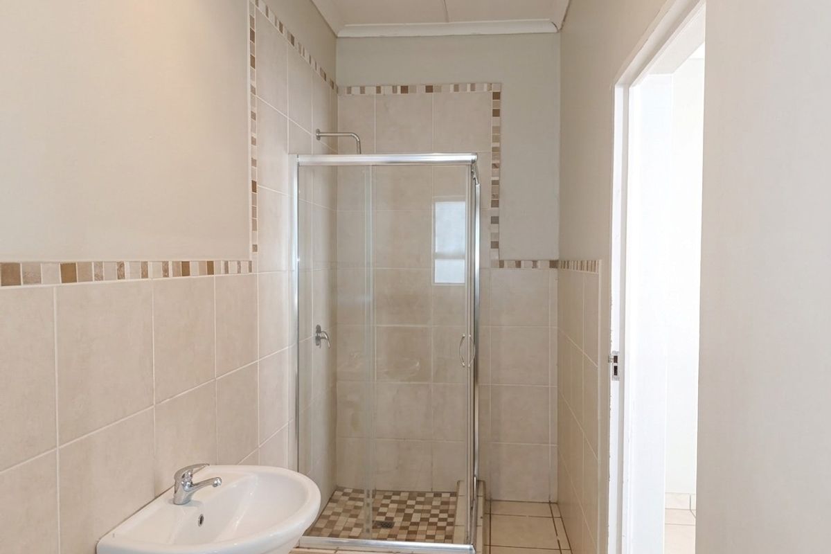 A clean and functional bathroom featuring a glass shower enclosure, pedestal basin, and neutral wall and floor tiling.