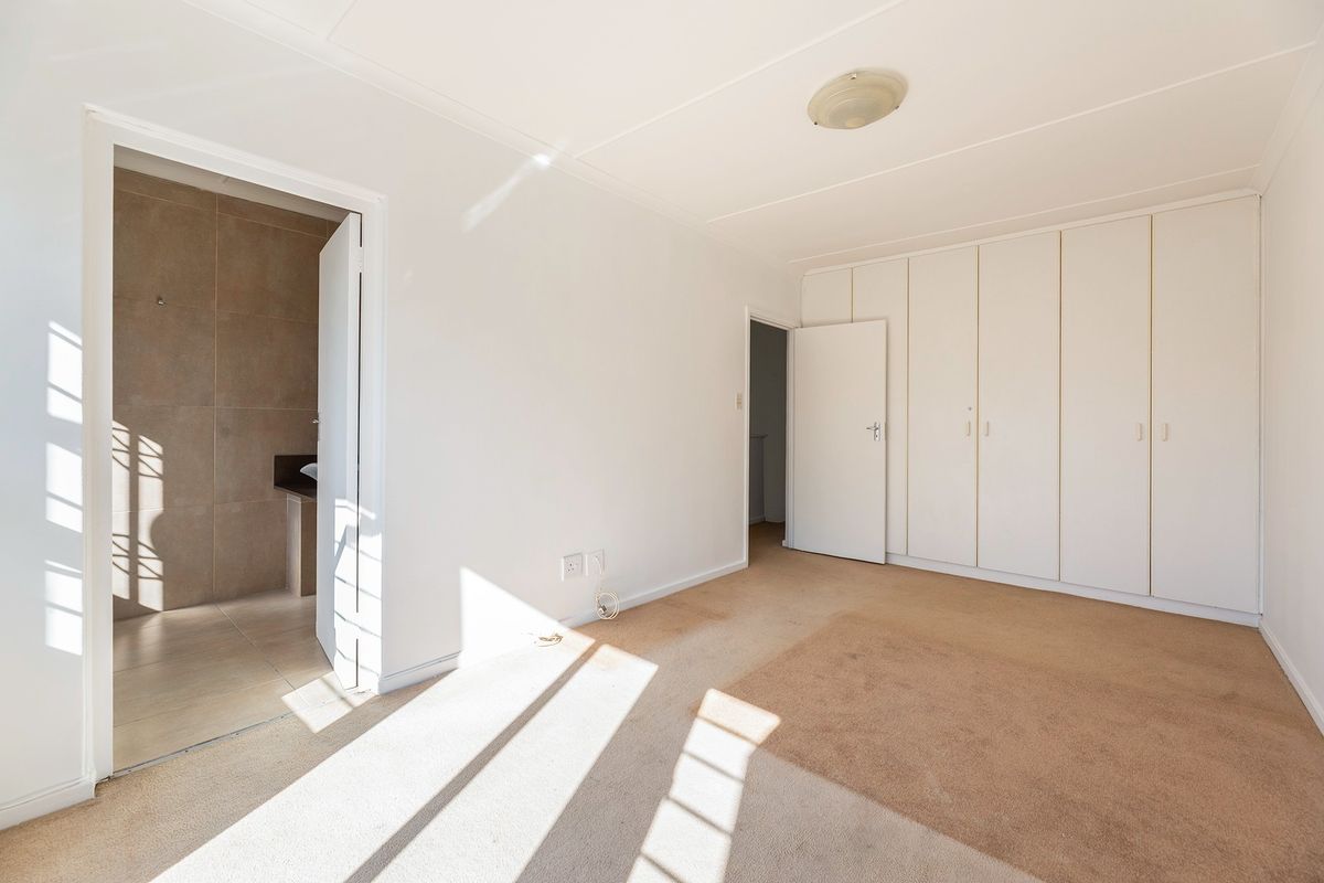 A spacious, empty bedroom featuring built-in cupboards, carpeted flooring, and direct access to an en-suite bathroom.