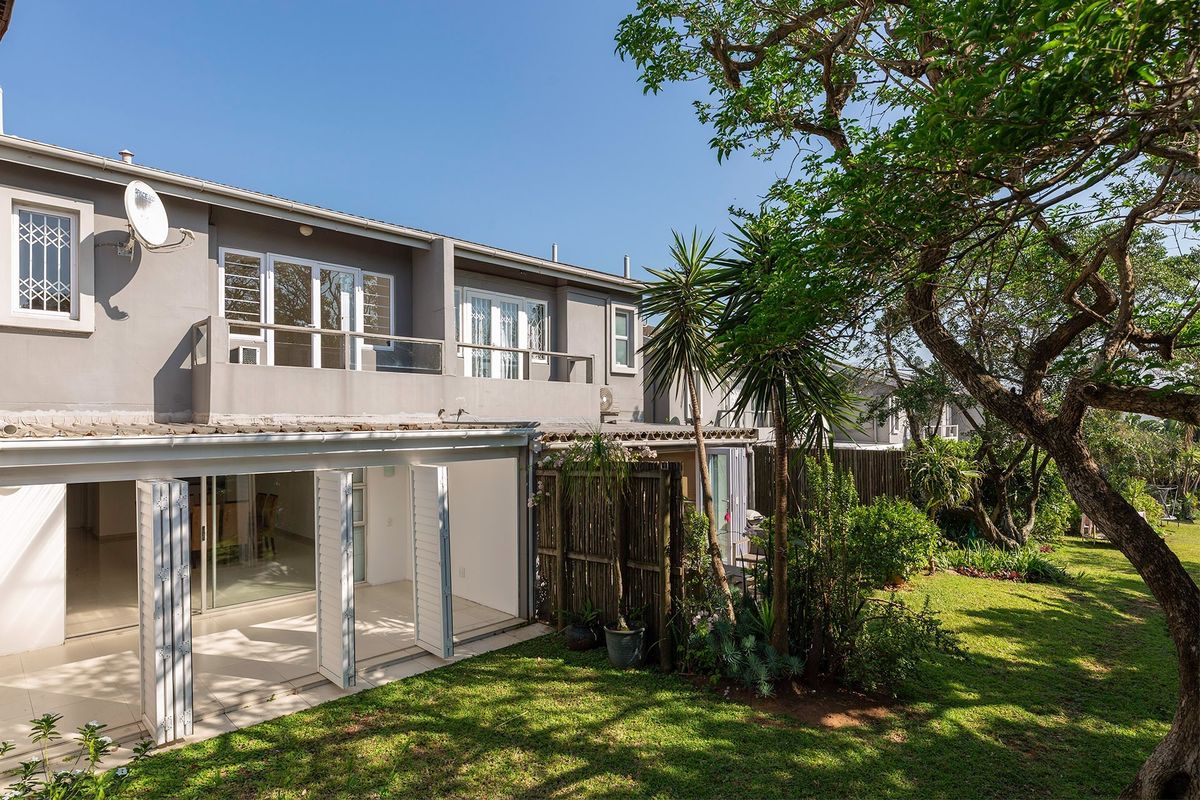 Rear view of the townhouse featuring a covered patio with folding doors, an upper-level balcony, and a well-maintained private garden.