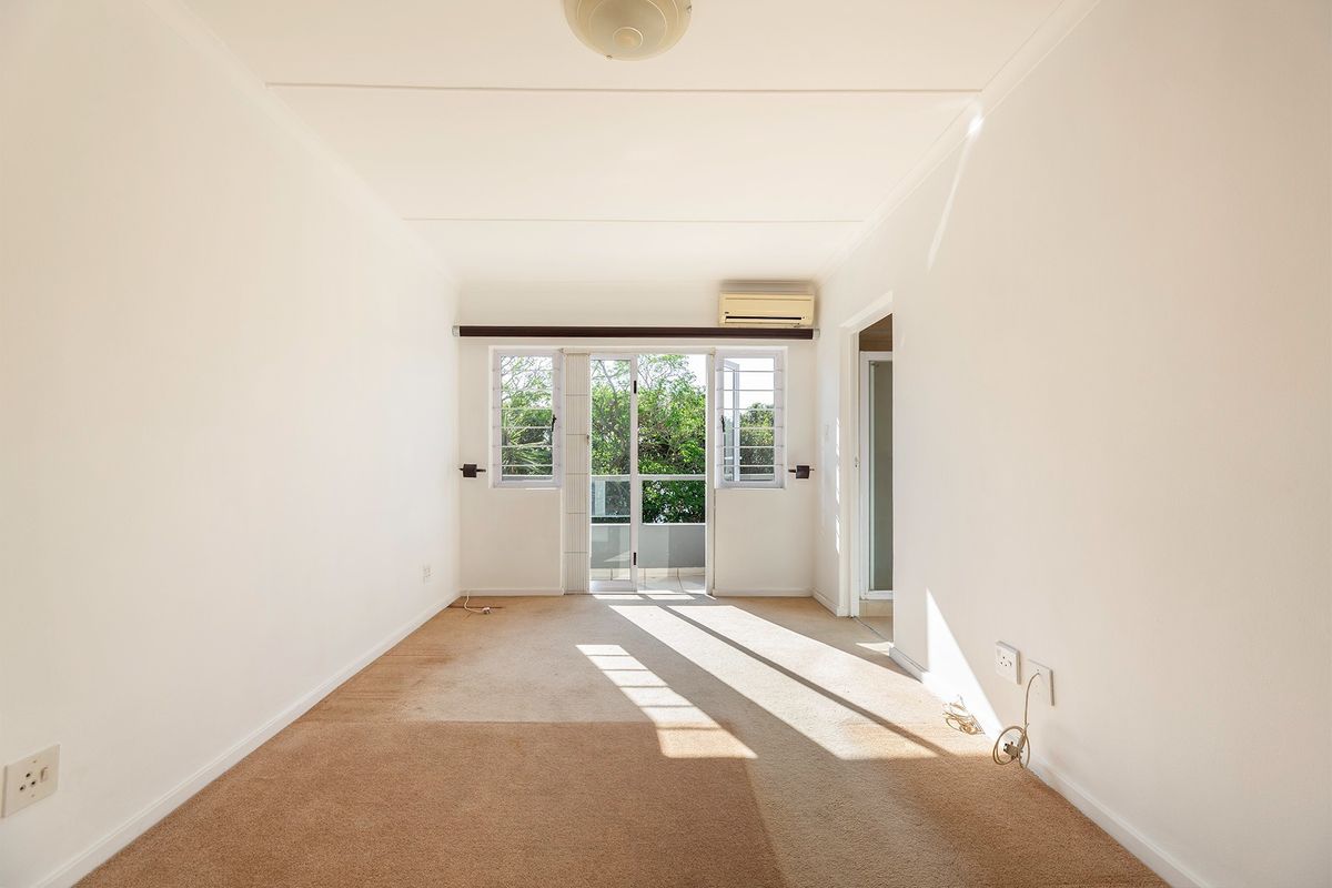 A bright, empty living room featuring carpeted flooring, an air conditioning unit, and a sliding glass door leading to an outdoor area.