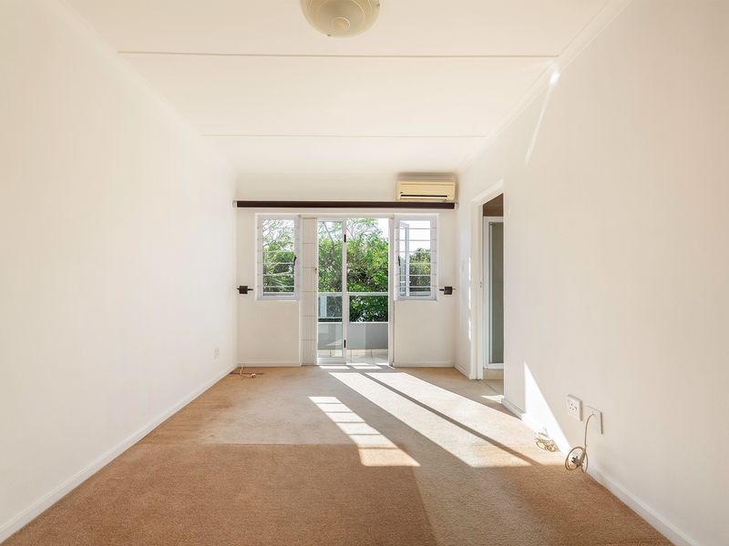 A bright, empty living room featuring carpeted flooring, an air conditioning unit, and a sliding glass door leading to an outdoor area.