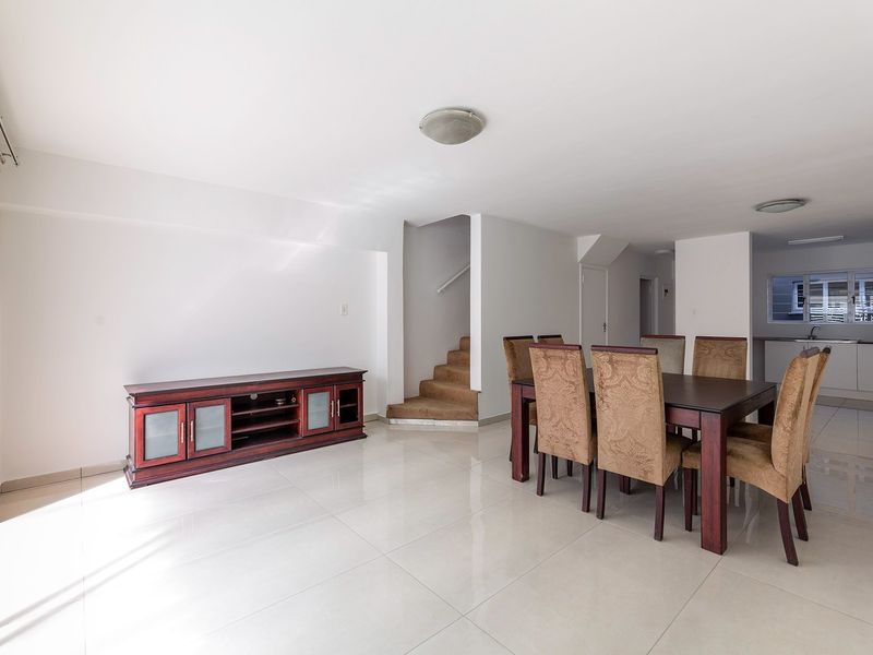 Spacious open-plan living and dining area featuring tiled flooring, a staircase, and a view through to the kitchen area.