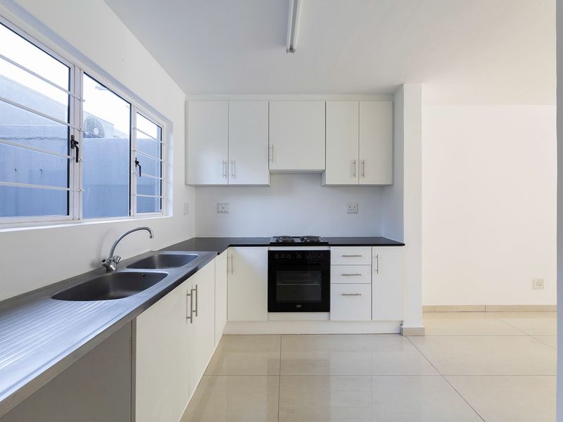 A clean, modern kitchen featuring white cabinetry, a stainless steel double sink, built-in oven and hob, and neutral tiled flooring.