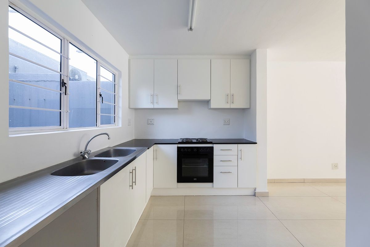 A clean, modern kitchen featuring white cabinetry, a stainless steel double sink, built-in oven and hob, and neutral tiled flooring.