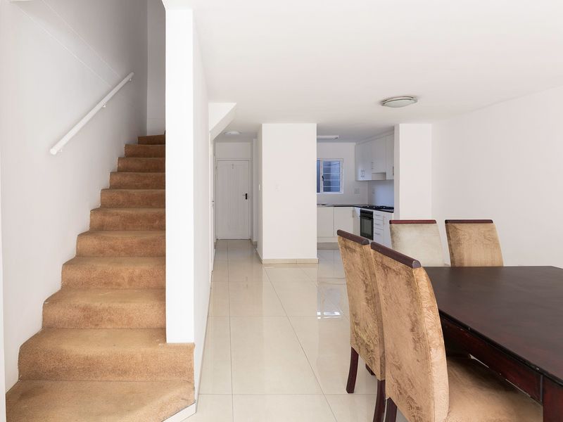 Open plan living and dining area featuring tiled floors, a carpeted staircase, and a functional kitchen with built-in cabinetry and appliances.