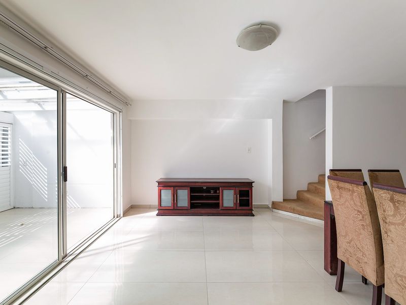 Open plan living area featuring large sliding glass doors leading to a patio, tiled flooring, and a staircase with carpeted steps.