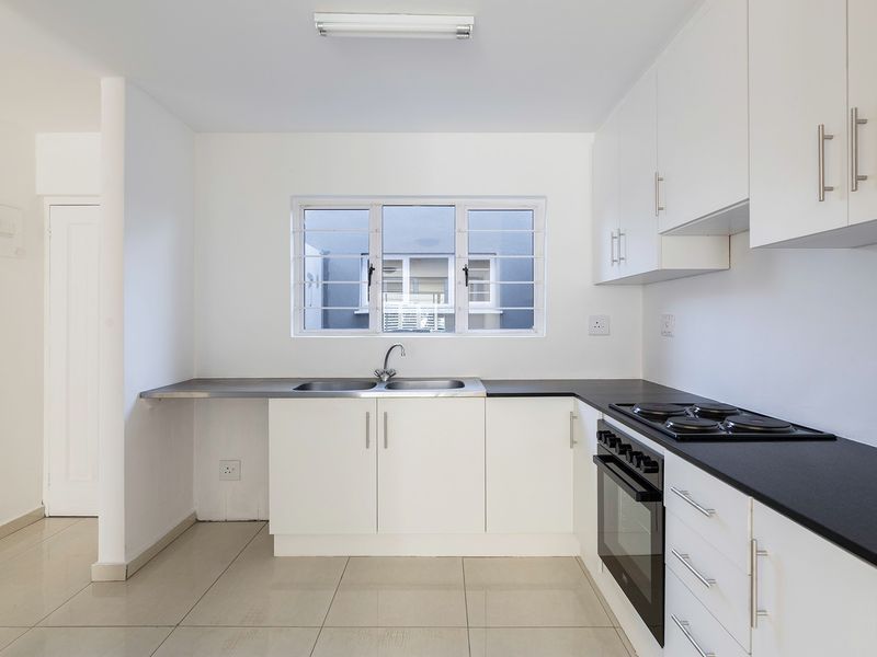 A clean and functional kitchen featuring white cabinetry, black countertops, a built-in oven and hob, and tiled flooring.