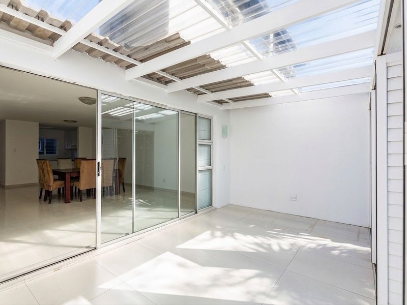 A bright, covered patio area featuring a translucent roof, tiled flooring, and large sliding glass doors providing seamless access to the interior living space.