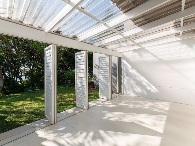 A bright, covered patio area featuring tiled flooring, bi-fold shutters, and a translucent roof, providing seamless access to the garden.