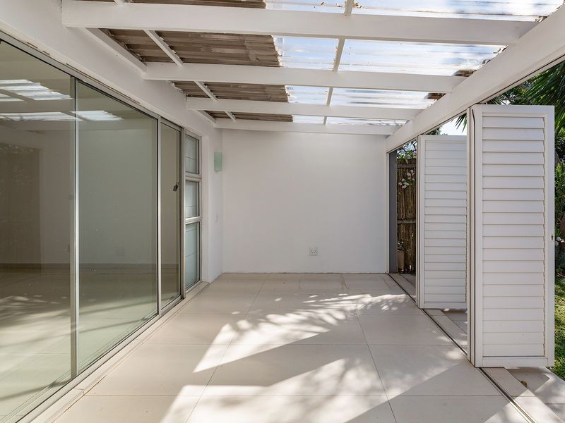 A covered patio area featuring tiled flooring, sliding glass doors, and white louvre shutters, providing a seamless transition to the garden.