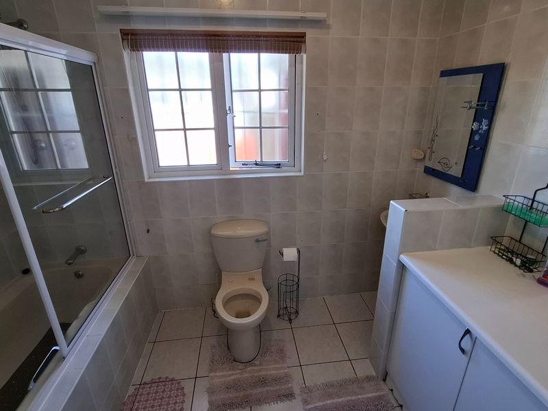 A functional bathroom featuring a shower-over-bath combination, a vanity unit with storage, and tiled finishes throughout.