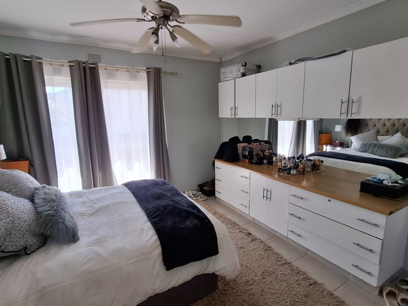 A well-lit bedroom featuring built-in white cabinetry with integrated mirrors, a ceiling fan, and tiled flooring, offering ample storage space.