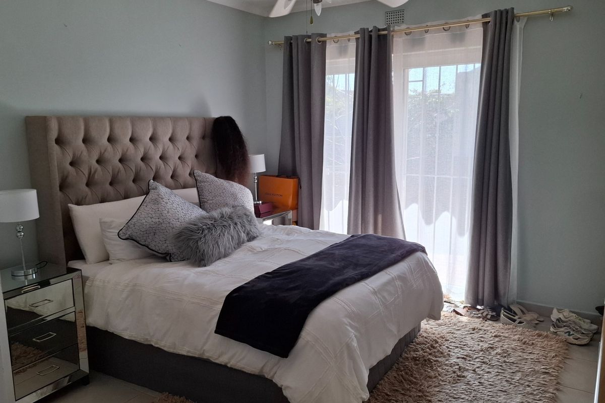 A well-lit bedroom featuring tiled flooring, a ceiling fan, and a sliding glass door with an integrated security gate providing access to the exterior.