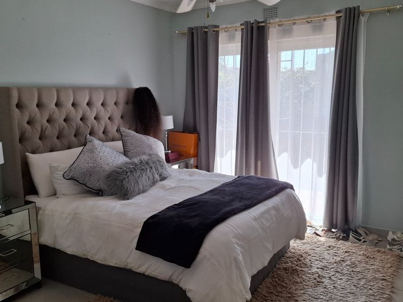 A well-lit bedroom featuring tiled flooring, a ceiling fan, and a sliding glass door with an integrated security gate providing access to the exterior.