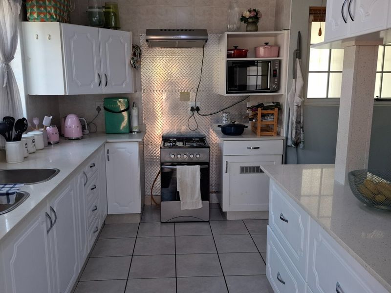 A functional kitchen featuring white cabinetry, stone countertops, a stainless steel gas stove with extractor fan, and a double basin sink.