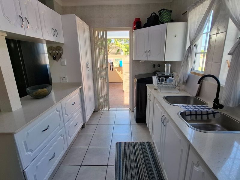 A functional kitchen featuring white cabinetry, laminate countertops, double stainless steel sinks, and tiled flooring, with direct access to an outdoor area.