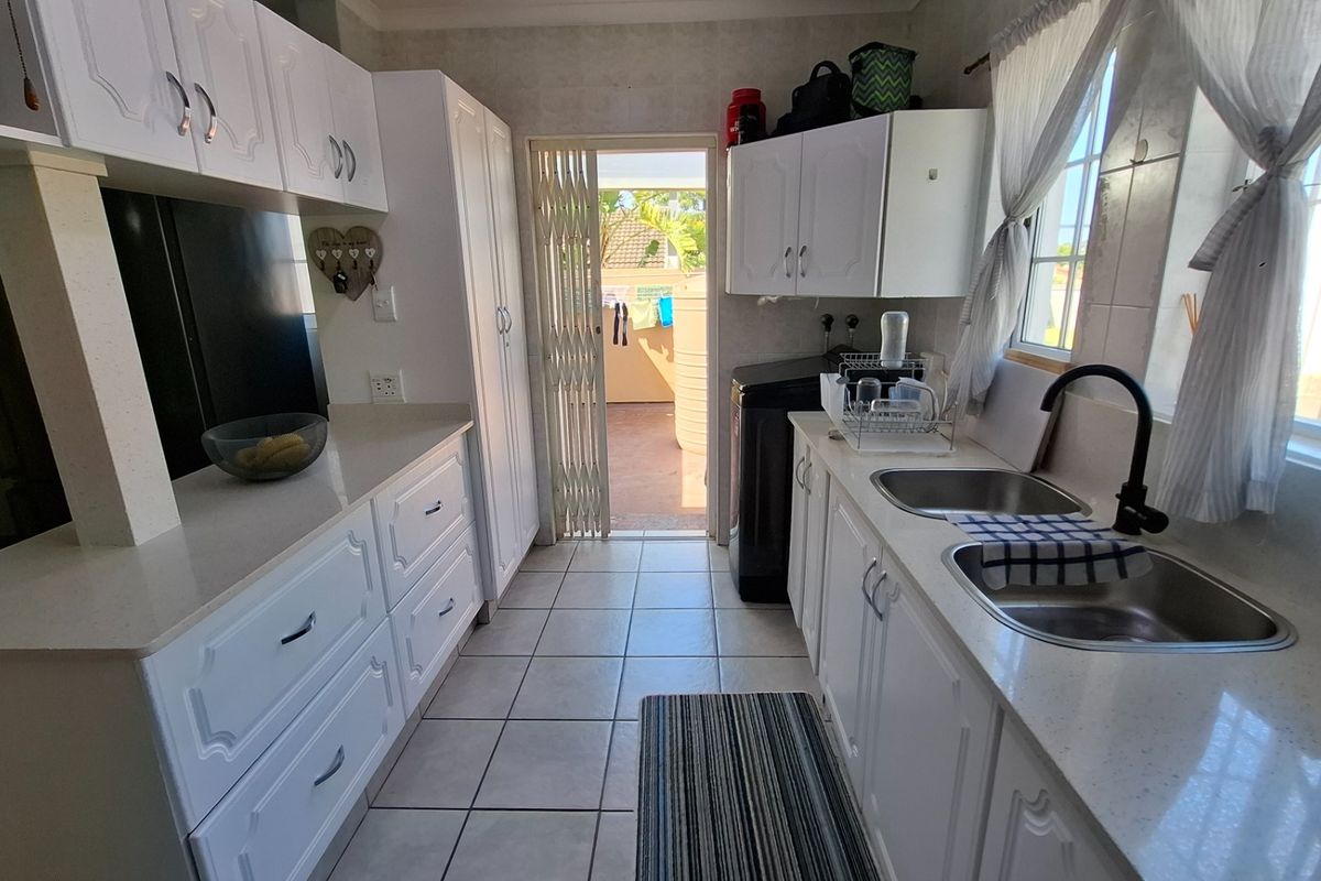 A functional kitchen featuring white cabinetry, laminate countertops, double stainless steel sinks, and tiled flooring, with direct access to an outdoor area.
