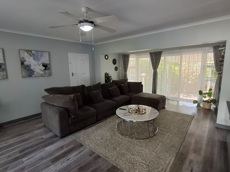 A well-maintained living room featuring modern laminate flooring, a ceiling fan, and large sliding glass doors that provide ample natural light.