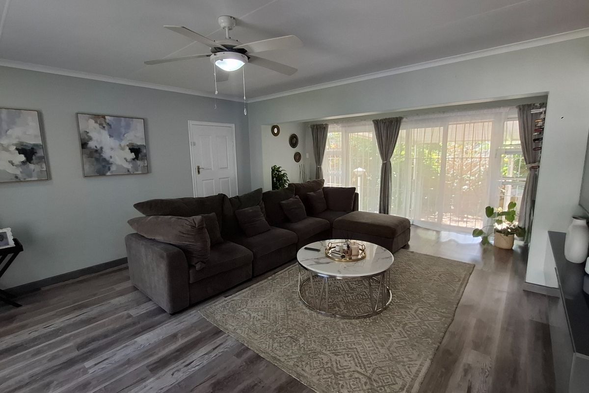 A well-maintained living room featuring modern laminate flooring, a ceiling fan, and large sliding glass doors that provide ample natural light.