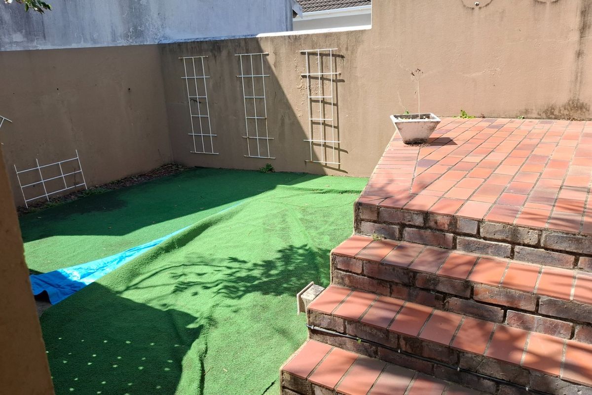 A private rear courtyard featuring brick stairs leading to an artificial lawn area with boundary walls and mounted trellis panels.