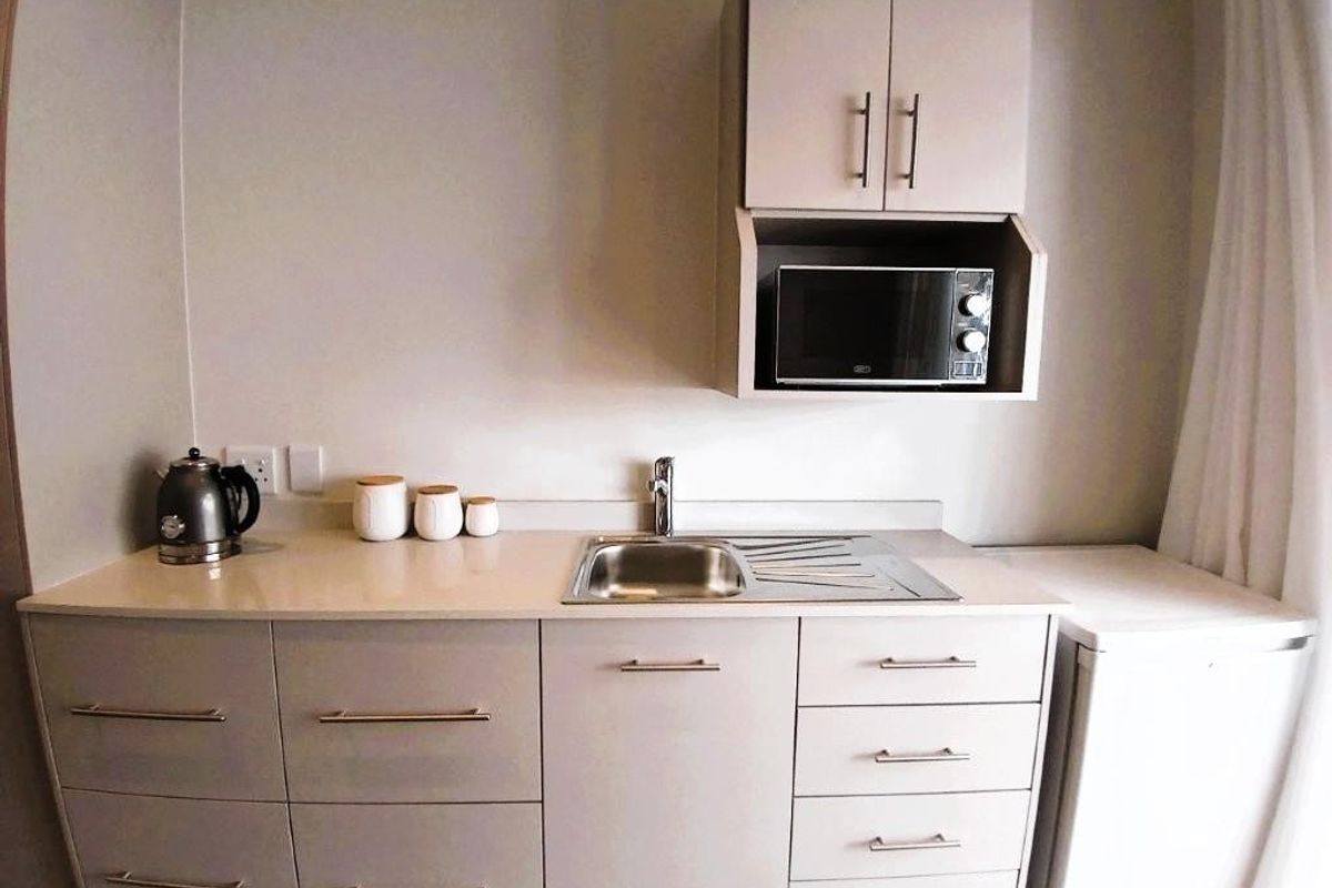 Compact kitchenette featuring modern cabinetry, stone countertops, a stainless steel sink, and a built-in microwave, providing efficient utility in a small space.