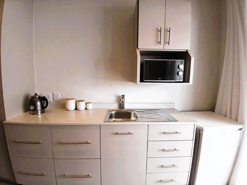 Compact kitchenette featuring modern cabinetry, stone countertops, a stainless steel sink, and a built-in microwave, providing efficient utility in a small space.