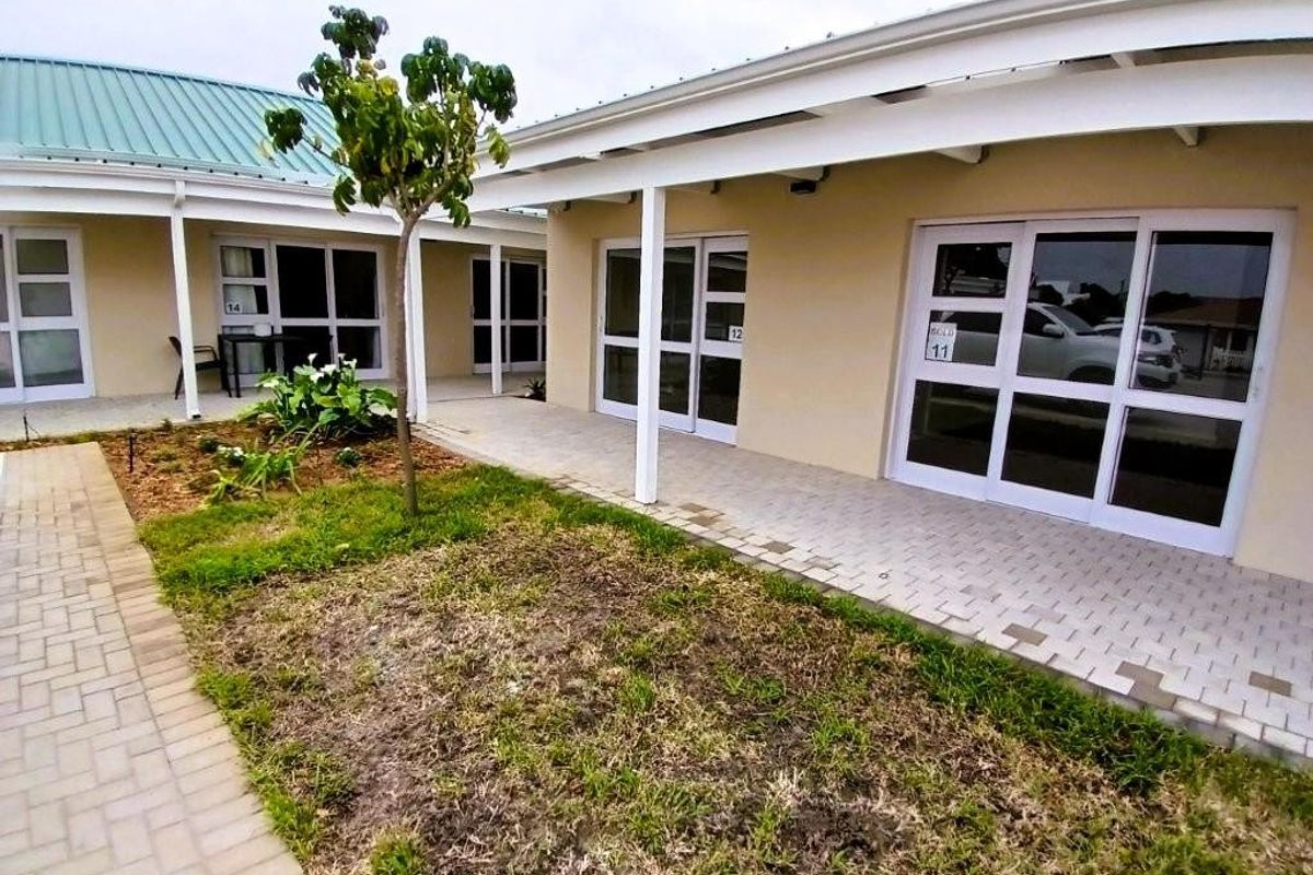 Exterior view of apartment units featuring covered patios, paved walkways, and sliding glass door access.