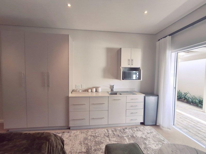 A compact kitchenette area featuring built-in cabinetry, a stainless steel sink, and a built-in microwave, with direct access to an outdoor patio.