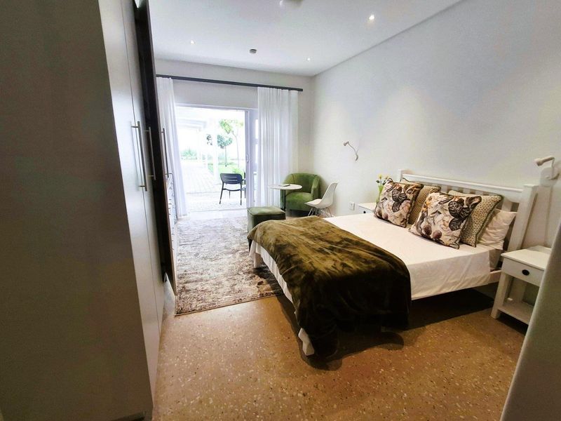 A well-lit bedroom featuring terrazzo flooring, built-in wardrobes, and direct access to an outdoor patio area through sliding glass doors.
