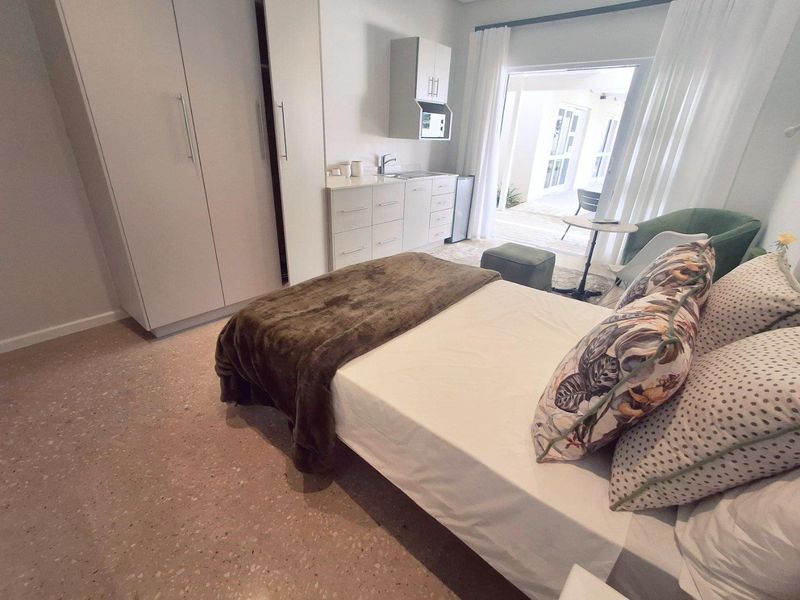 A well-maintained bedroom featuring built-in cupboards, a compact kitchenette area with sink, and direct access to an outdoor patio through sliding glass doors.
