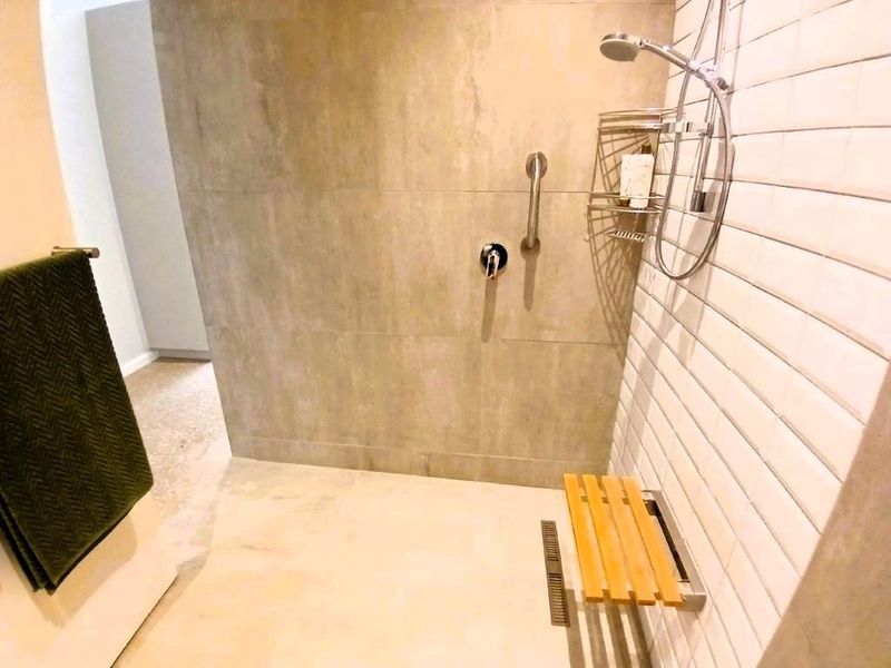 Modern walk-in shower featuring large format tiling, subway tile accents, a built-in wooden bench, and a convenient grab rail for accessibility.