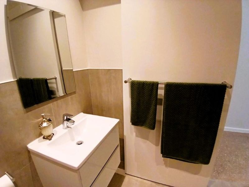 A modern bathroom featuring a sleek vanity cabinet with a ceramic basin, chrome mixer tap, and a wall-mounted mirror with tiled splashback.