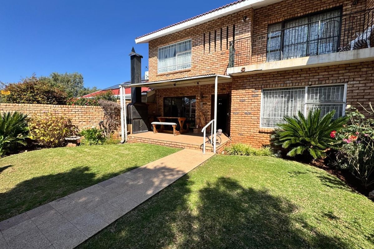 Rear view of a brick townhouse featuring a covered patio with a built-in braai, a paved walkway, and a private garden area.