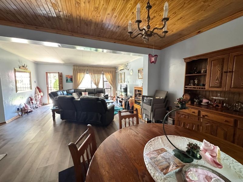 Spacious open-plan living and dining area featuring warm timber ceiling finishes, laminate flooring, and a split-system air conditioner for climate control.