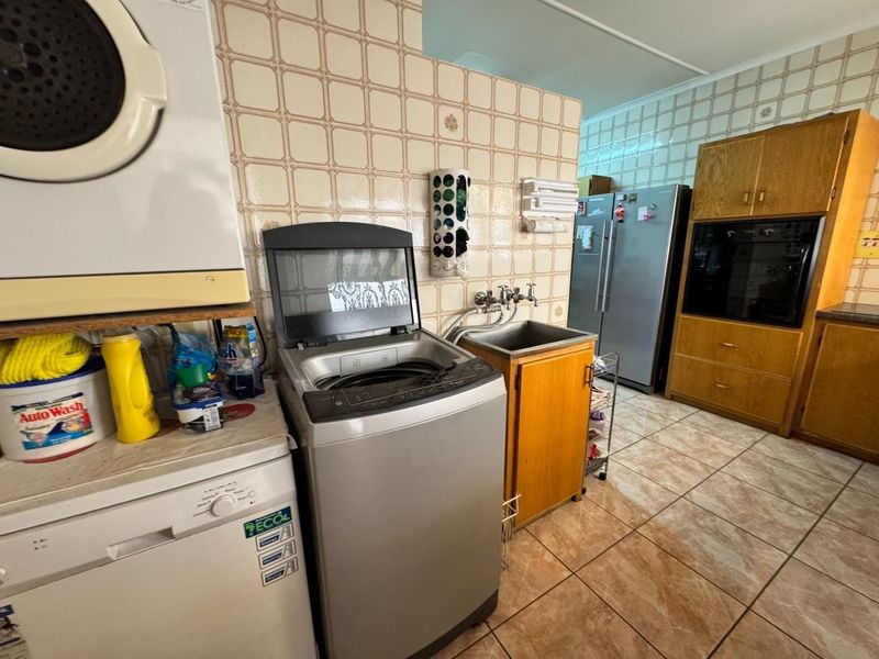A functional laundry area featuring tiled walls, built-in cabinetry, a utility sink, and integrated oven space, offering potential for modernization.