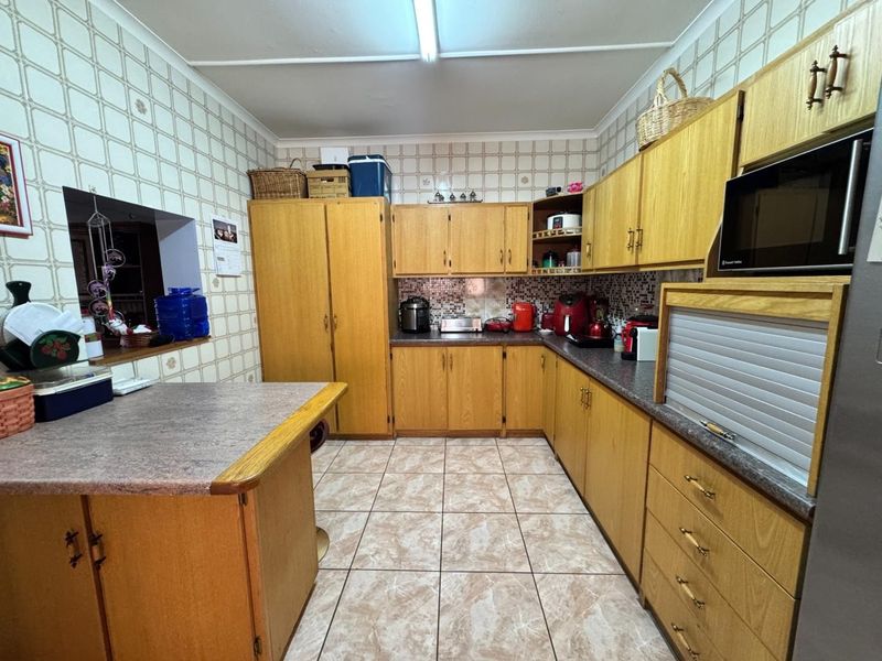 A functional kitchen featuring extensive laminate cabinetry, laminate countertops, mosaic tile backsplash, and ceramic floor tiles with a convenient pass-through window.