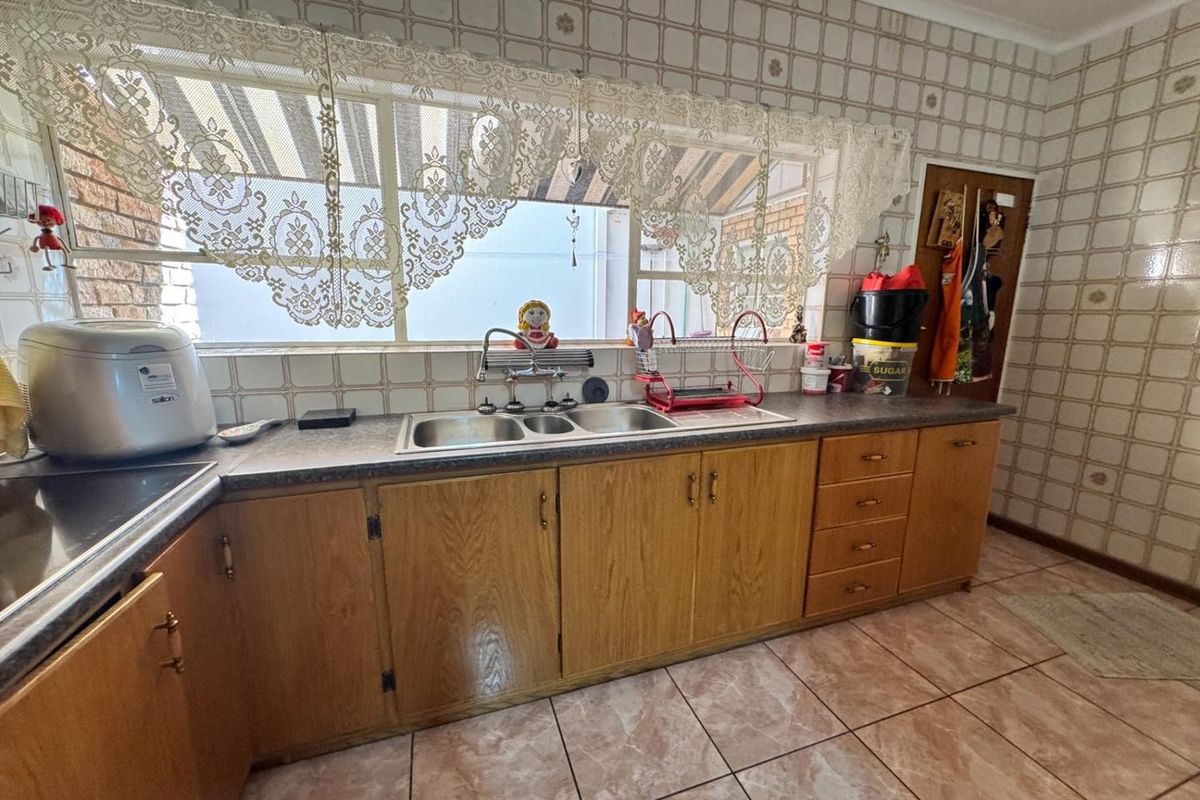 A dated kitchen featuring wooden cabinetry, laminate countertops, a double basin sink, and tiled splashbacks, offering potential for a modern renovation.