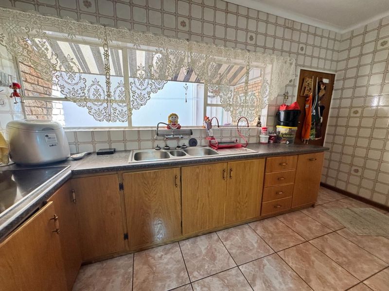 A dated kitchen featuring wooden cabinetry, laminate countertops, a double basin sink, and tiled splashbacks, offering potential for a modern renovation.