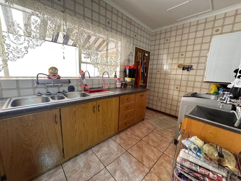 A functional kitchen featuring wooden cabinetry, laminate countertops, a double bowl sink, and tiled finishes throughout, offering potential for modernization.