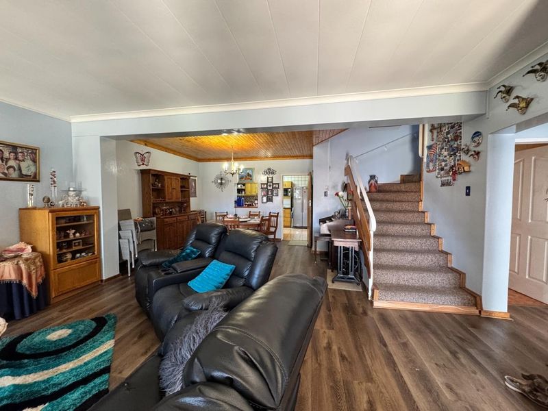 Open plan living and dining area featuring laminate flooring, a staircase with carpeted treads, and a wooden ceiling section in the dining space.