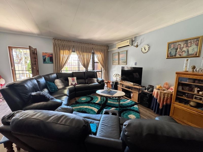 A comfortable living room featuring laminate flooring, a wall-mounted air conditioning unit, and security features on the windows and entrance door.