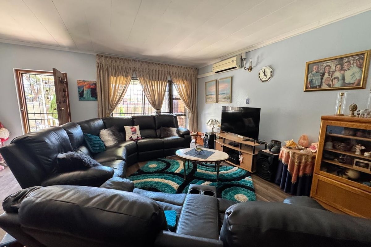 A comfortable living room featuring laminate flooring, a wall-mounted air conditioning unit, and security features on the windows and entrance door.
