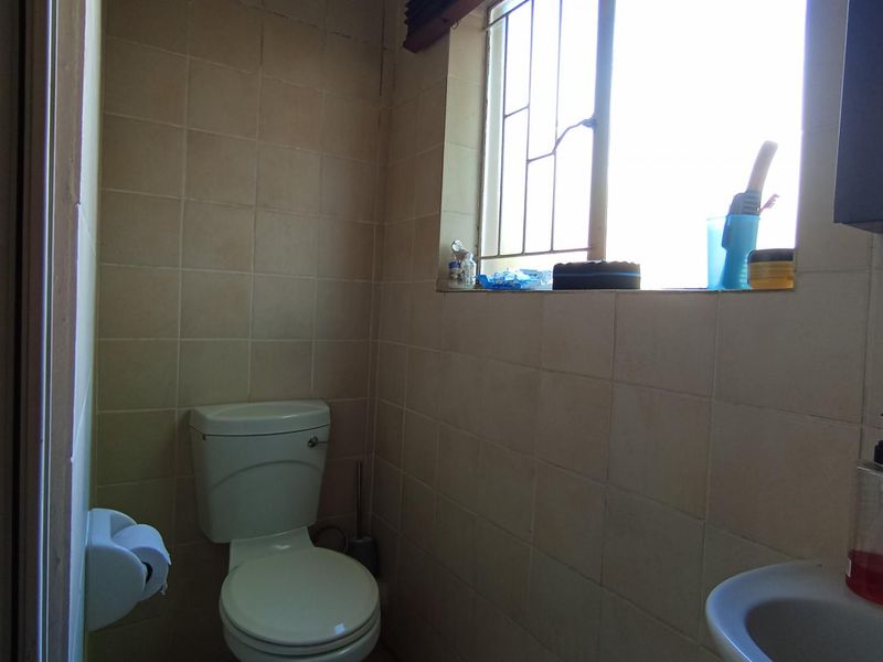 A functional bathroom featuring a standard toilet, wall-mounted washbasin, and neutral ceramic wall tiling with a window for natural light.