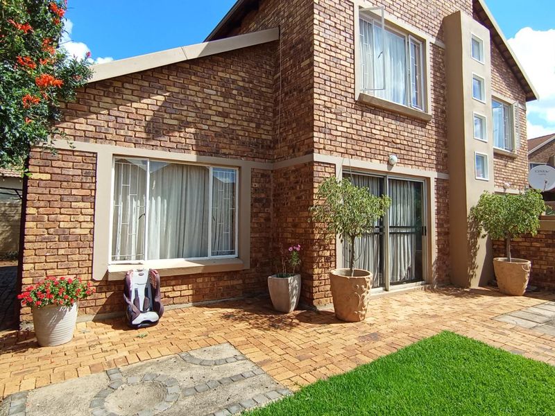 A well-maintained rear exterior view of a face brick house featuring a paved patio area and sliding glass door access.